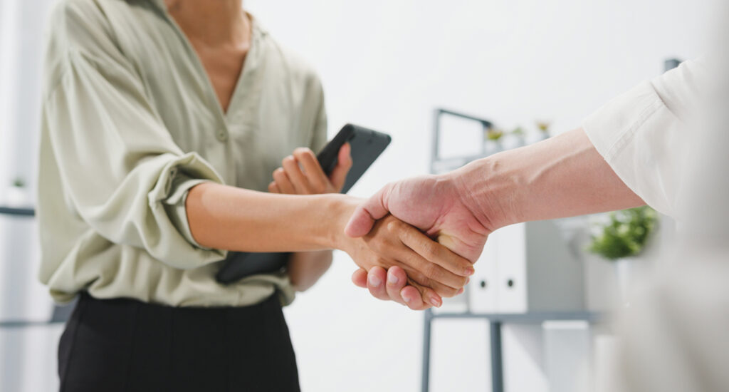Multiracial group of young creative people in smart casual wear discussing business shaking hands together and smiling while standing in modern office. Handshake