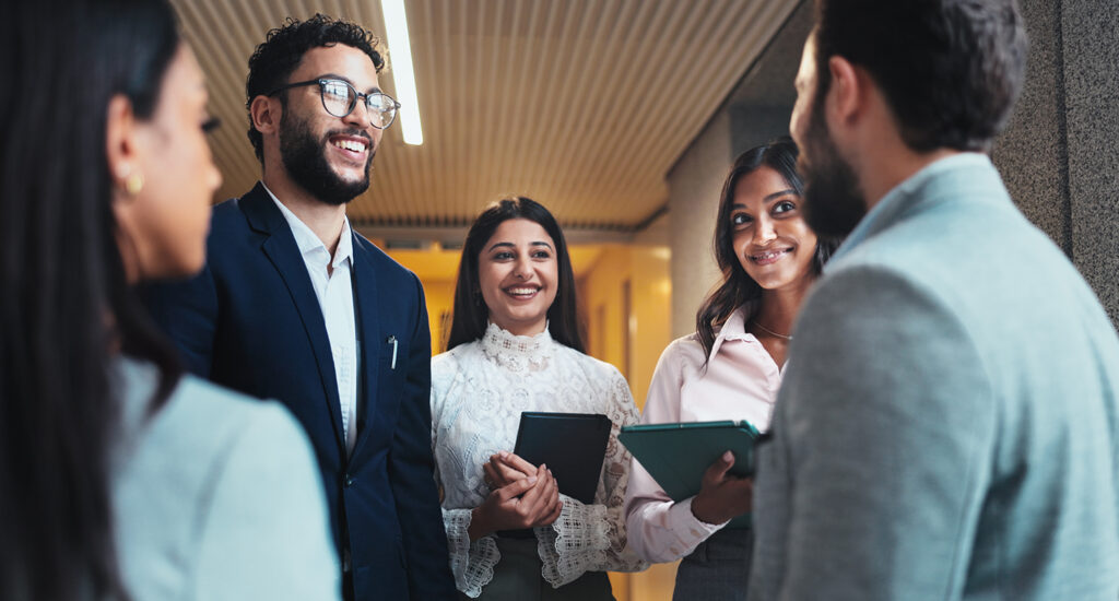 Group of colleagues standing in hallway talking and smiling.