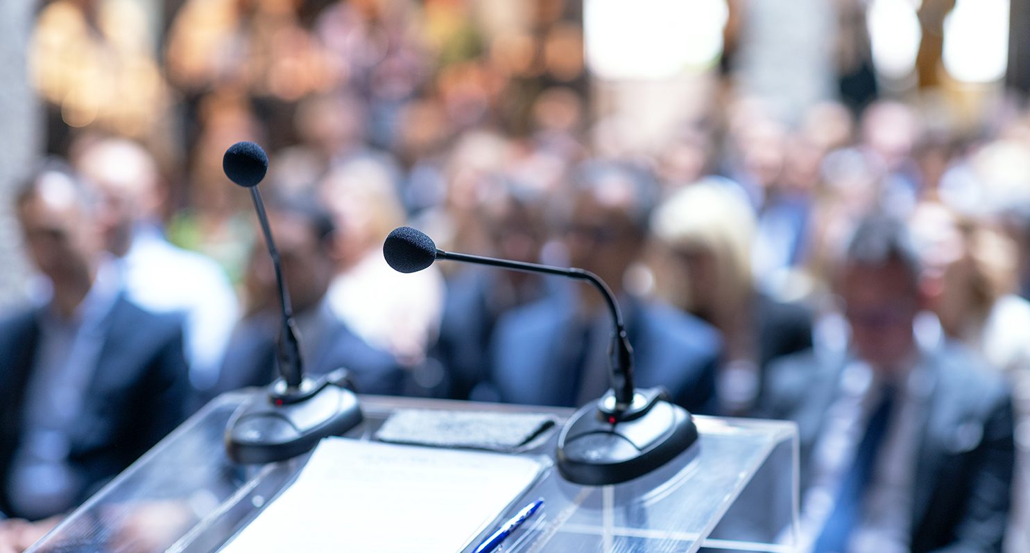 Close up microphone and podium on stage in large meeting room.